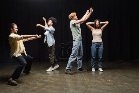 full length of young and emotional students rehearsing in theater school