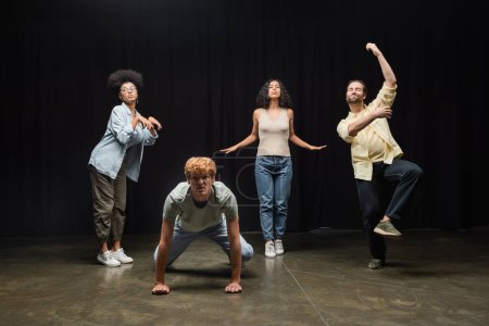 full length of multiethnic actors rehearsing in different poses on stage in theater