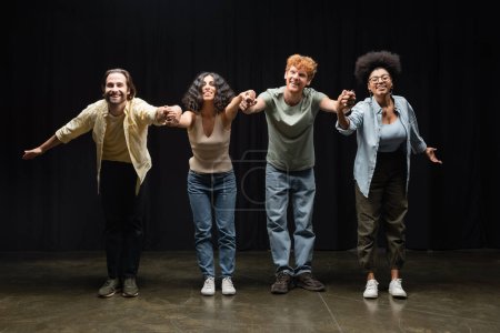 Foto de Full length of happy multiethnic actors holding hands and bowing on stage of theater - Imagen libre de derechos
