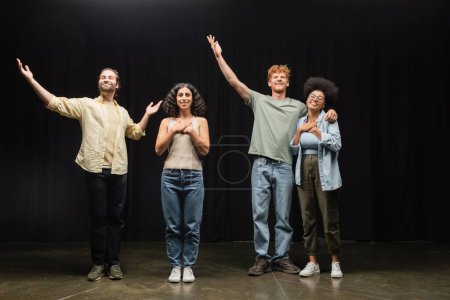 Foto de Full length of happy multiethnic actors standing with raised hands on scene of theater - Imagen libre de derechos