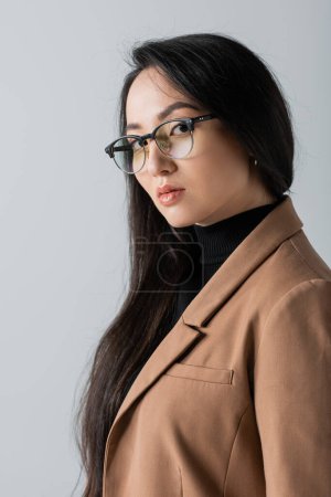 Foto de Young asian businesswoman in glasses and blazer looking at camera isolated on grey - Imagen libre de derechos