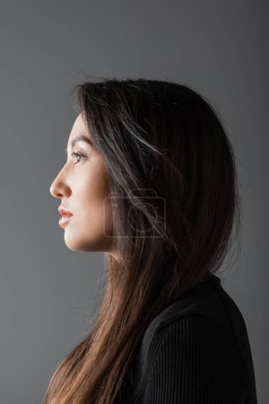 Téléchargez les photos : Side view of brunette and asian woman in black turtleneck looking away isolated on dark grey - en image libre de droit