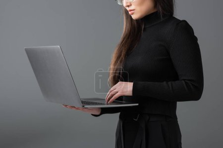 cropped view of woman in black turtleneck using laptop isolated on dark grey 