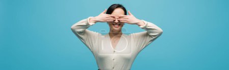 Photo for Positive brunette woman covering face isolated on blue, banner - Royalty Free Image