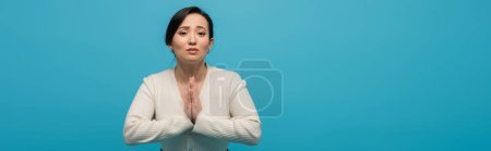 Brunette asian woman showing hope gesture isolated on blue, banner 