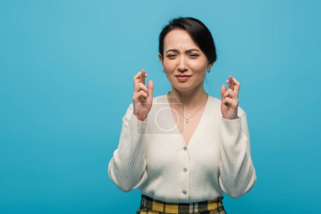 Young asian woman crossing fingers isolated on blue 