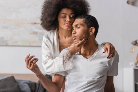 Photo for Sexy african american woman with curly hair and closed eyes touching face of young boyfriend in bedroom - Royalty Free Image