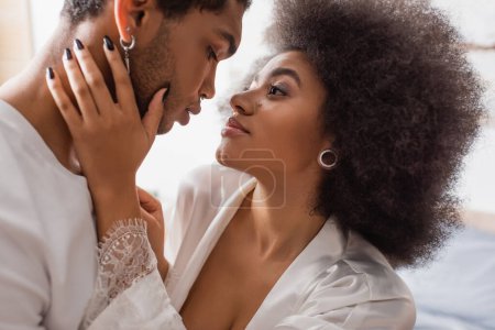 Photo for Sensual african american woman in white silk robe touching face of young boyfriend - Royalty Free Image