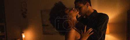 Téléchargez les photos : Vue latérale de l'homme afro-américain en chemise noire embrassant une femme passionnée dans une pièce sombre avec éclairage, bannière - en image libre de droit