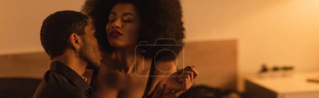Photo for Young man kissing curly and sexy african american girlfriend at home, banner - Royalty Free Image