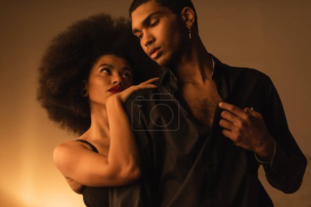 femme africaine américaine sensuelle embrassant jeune homme en chemise noire tout en le séduisant la nuit