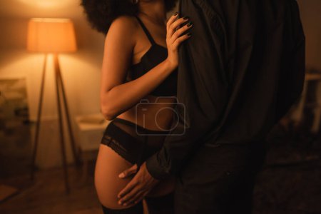 cropped view of man in black clothes near sexy african american girlfriend in black lingerie