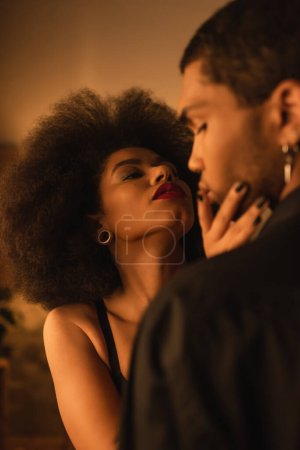femme afro-américaine passionnée toucher le visage du jeune homme tout en le séduisant à la maison