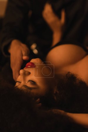 sexy african american woman with closed eyes near blurred man in dark bedroom