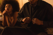 blurred african american woman looking at man unbuttoning black shirt in bedroom hoodie #637252938