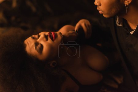 Foto de Passionate african american woman near young boyfriend in dark bedroom - Imagen libre de derechos