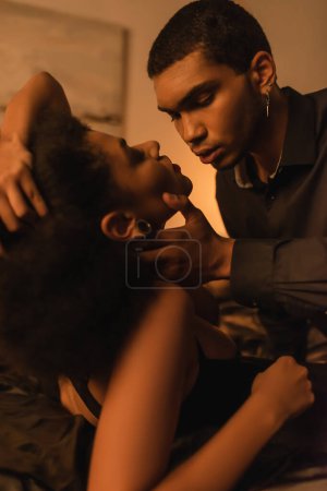 Foto de Young african american man touching neck of passionate girlfriend on bed - Imagen libre de derechos
