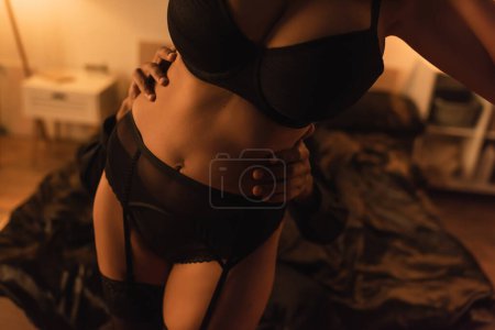 cropped view of sexy african american woman in black underwear near man embracing her in dark bedroom