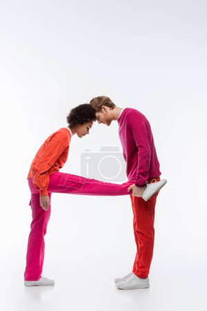 Téléchargez les photos : Vue latérale du couple interracial en vêtements de couleur magenta montrant une lettre sur fond blanc - en image libre de droit