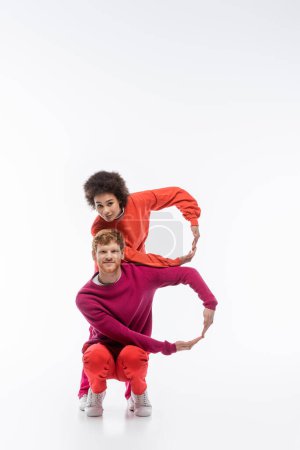fröhliches gemischtrassiges Paar in magentafarbener Kleidung, das einen Buchstaben mit Händen auf weißem Hintergrund zeigt 