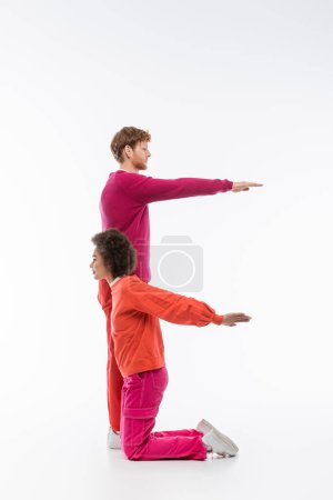 Photo for Side view of multiethnic man and woman in trendy magenta color clothes showing e letter on white background - Royalty Free Image