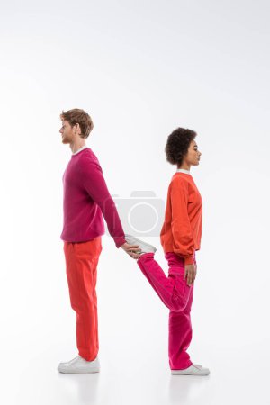 Téléchargez les photos : Vue latérale du couple interracial en vêtements de couleur magenta montrant n lettre sur fond blanc - en image libre de droit