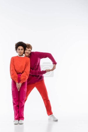 cheerful and multiethnic couple in magenta color clothes showing R letter on white background 
