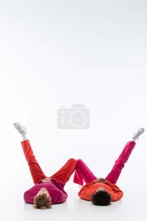 interracial couple in magenta color clothes lying on floor and showing w letter with legs on white background 