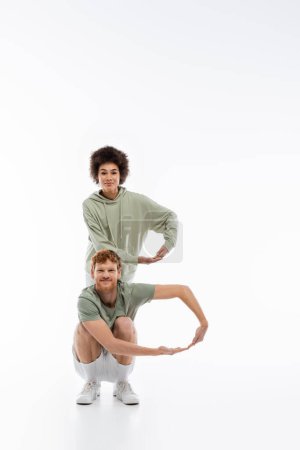 glückliches und gemischtrassiges Paar in pastellgrüner Kleidung, das den Buchstaben b auf weißem Hintergrund zeigt 