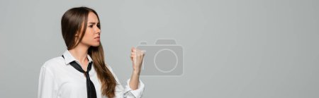 Téléchargez les photos : Jeune femme en colère en chemise blanche et cravate montrant poing serré isolé sur gris, bannière - en image libre de droit