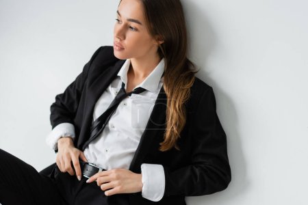 Foto de High angle view of young brunette woman in black formal wear touching belt on grey background - Imagen libre de derechos