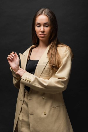 brunette young woman in beige suit standing and looking away on black 