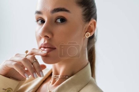 Foto de Close up view of young woman with sensual lips touching chin isolated on grey - Imagen libre de derechos
