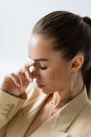 close up view of young woman with closed eyes touching nose isolated on grey 