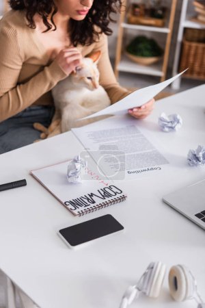 Téléchargez les photos : Cropped view of devices and papers near copywriter holding oriental cat at home - en image libre de droit