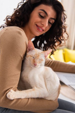 Smiling copywriter looking at oriental cat near documents at home 