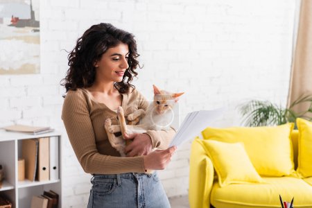 Copywriter positivo sosteniendo gato oriental y documentos en casa 