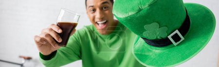 Téléchargez les photos : Happy african american man holding glass of dark beer and green hat on Saint Patrick Day, banner - en image libre de droit