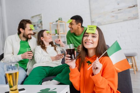 glückliche Frau mit königlichem Wort auf klebrigem Zettel mit irischer Flagge und einem Glas Bier in der Nähe ihrer Freunde am Saint Patrick Day