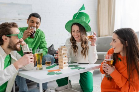 Cheerful multiethnic friends drinking beer and playing wood blocks game at home 