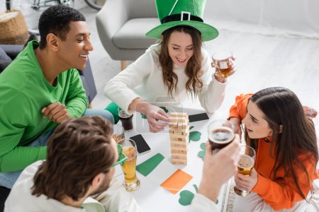 Overhead view of interracial friends with beer playing wood block game during saint patrick day at home 