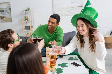 Positive interracial people clinking beer while celebrating saint patrick day at home 