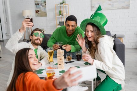 Multiethnic friends taking selfie while celebrating saint patrick day at home 