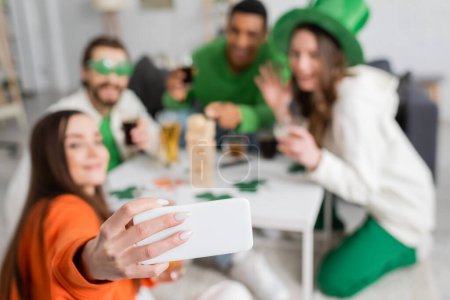 Verschwommene interrassische Freunde machen Selfie auf dem Smartphone, während sie den Patrick Day zu Hause feiern 
