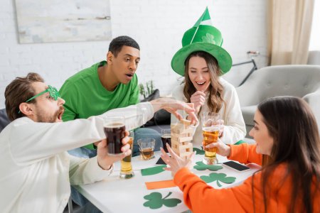 Aufgeregt multiethnische Freunde mit Bier spielen Holzklötze Spiel am Saint-Patrick-Tag 