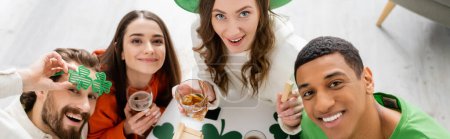 Overhead view of cheerful interracial friends with beer celebrating saint patrick day at home, banner 