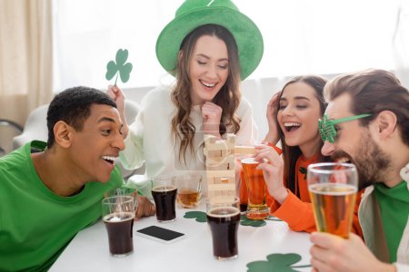 Positive multiethnic friends with beer playing wood blocks game during saint patrick day