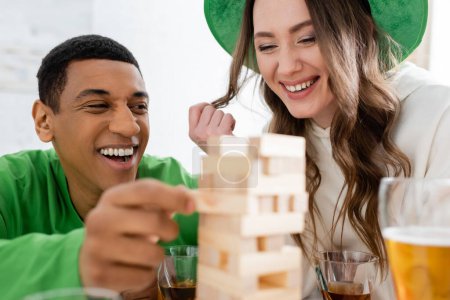 Cheerful multiethnic friends playing blurred wood blocks game during saint patrick day