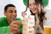 Cheerful multiethnic friends playing blurred wood blocks game during saint patrick day t-shirt #639066440