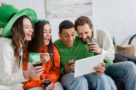 Positive multiethnische Freunde beim Bier mit digitalem Tablet zu Hause 